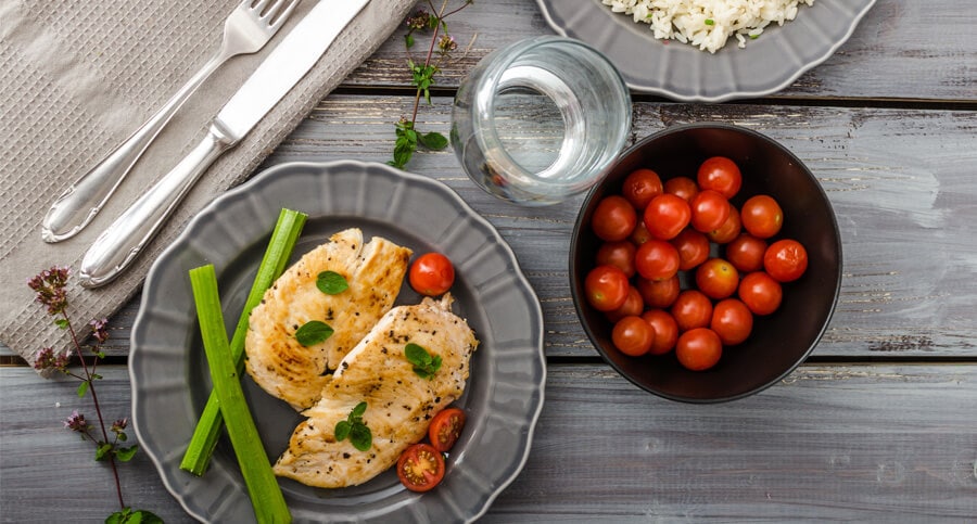 Mesa posta com prato cinza, servido com filé de frango, tomate cereja e nabo, representando a dieta para ectomorfo.