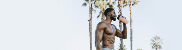 Imagem sobre dieta para ectomorfo, com homem negro, sem camisa, segurando uma coqueteleira. Ao fundo, há céu azul e árvores.