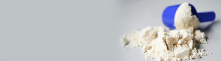 Medidor azul com um pouco de pó branco espalhado em superfície cinza. Imagem para explicar para que serve a maltodextrina.