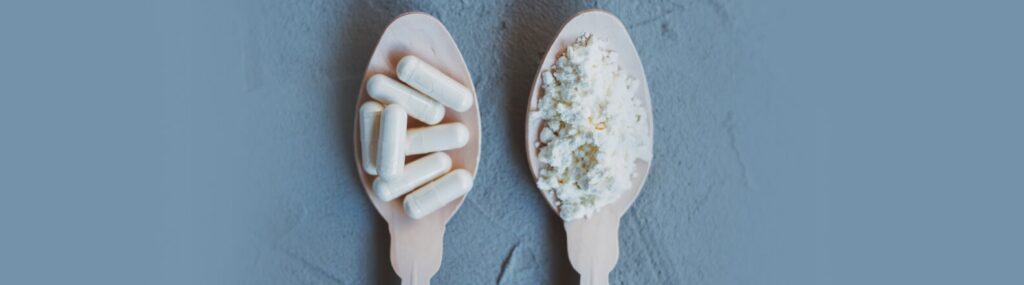 duas colheres em cima da mesa, uma como colostro bovino em pó e a outra com capsulas