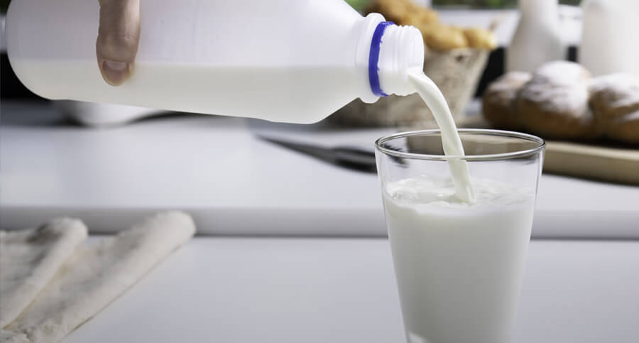 pessoa enchendo copo de leite em cima da mesa para explicar o que é intolerância a lactose