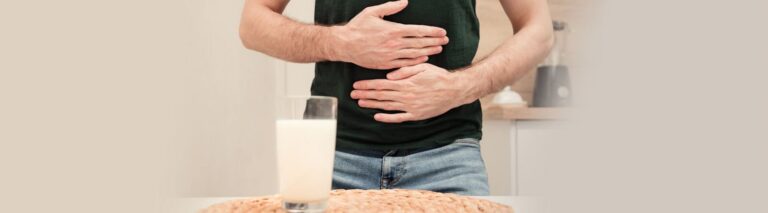 homem com a mão na barriga em frente a um copo de leite pensando sobre o que é intolerância a lactose.