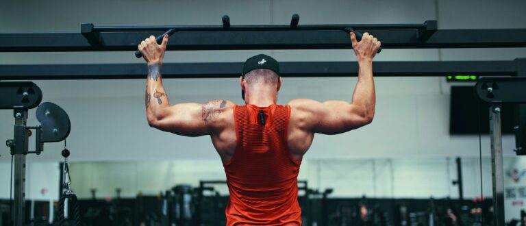 Homem realizando barra fixa em academia, com foco no fortalecimento da musculatura das costas e dos braços. Treino de força utilizado em fases de ganho e definição muscular como bulking e cutting.