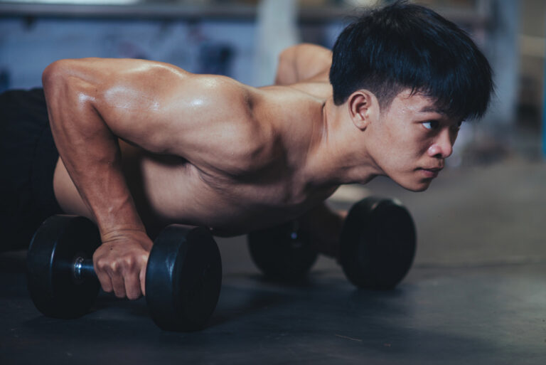 Homem realizando flexão de braços com apoio em halteres durante treino de musculação. Exercício de força relacionado à manutenção da massa muscular e à prevenção do catabolismo muscular.
