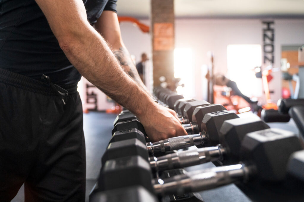 Homem segurando halteres em academia durante treino de força. Dias sem treinar podem impactar a performance e a manutenção da massa muscular.