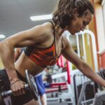Mulher realizando exercício de força na academia como preparação para campeonatos de fisiculturismo feminino.