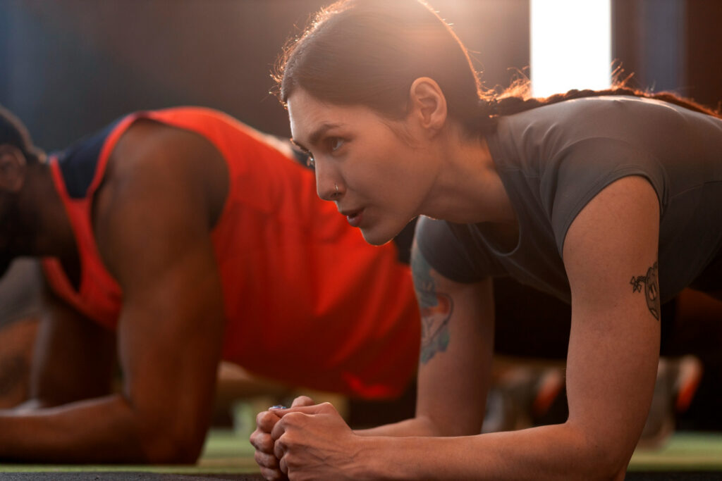 Mulher realizando prancha durante treino regenerativo em ambiente de academia, com foco na recuperação muscular, redução da fadiga e melhora da performance esportiva após treinos intensos.