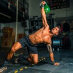 Atleta executando levantamento com kettlebell em sessão de treino full body, método que estimula todos os grupos musculares, promovendo ganhos de força e hipertrofia.