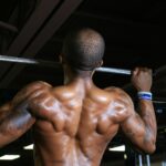 Homem treinando costas em barra fixa na academia para manutenção da massa muscular durante o processo de emagrecimento.
