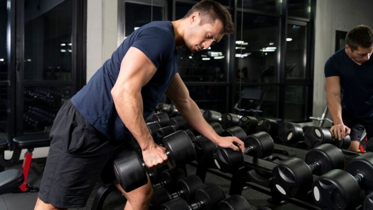Homem executando remada unilateral com halter na academia para fortalecimento das costas e equilíbrio muscular.